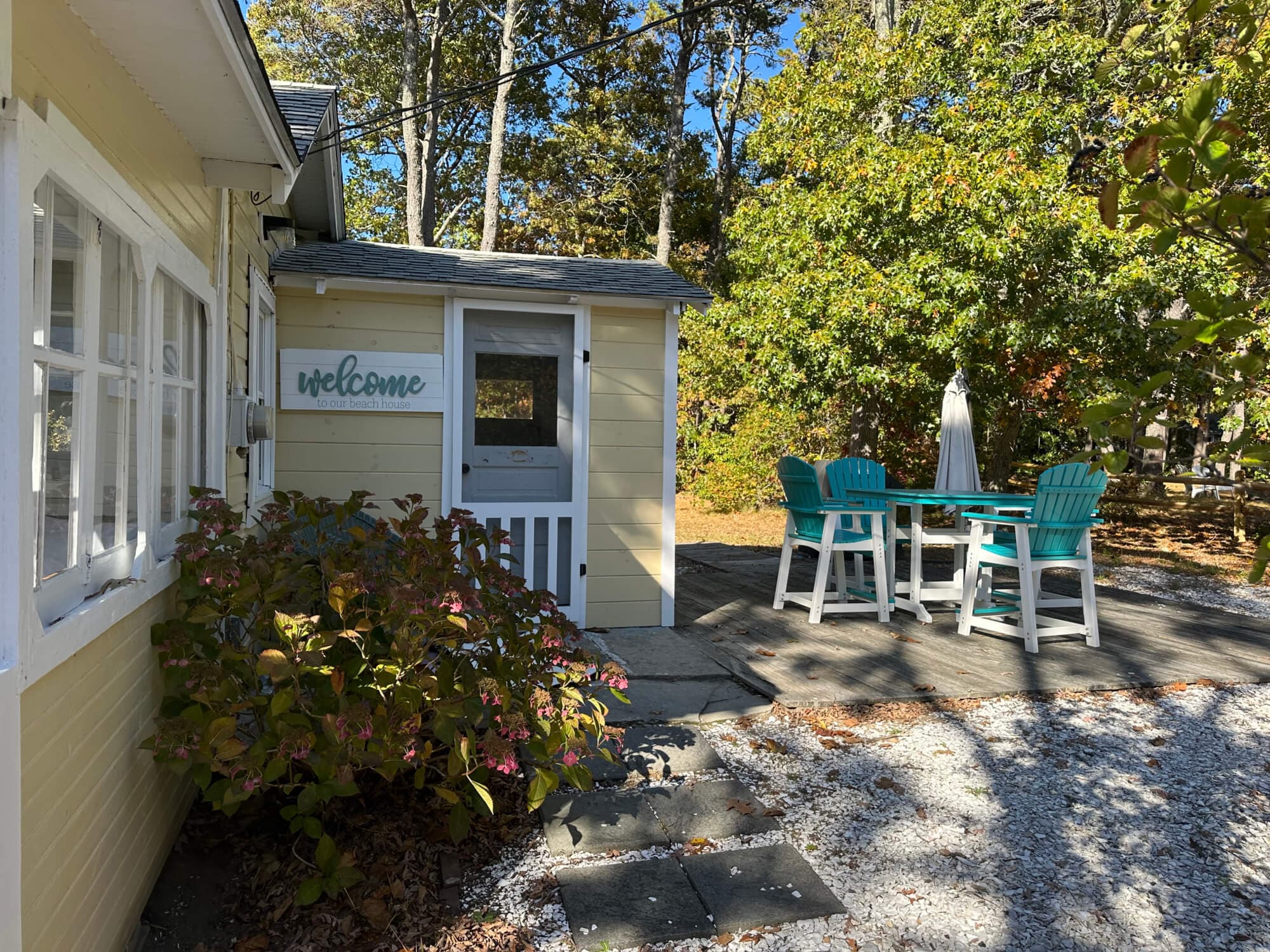 A cheerful entrance to a home with a "welcome" sign and outdoor seating amid trees.