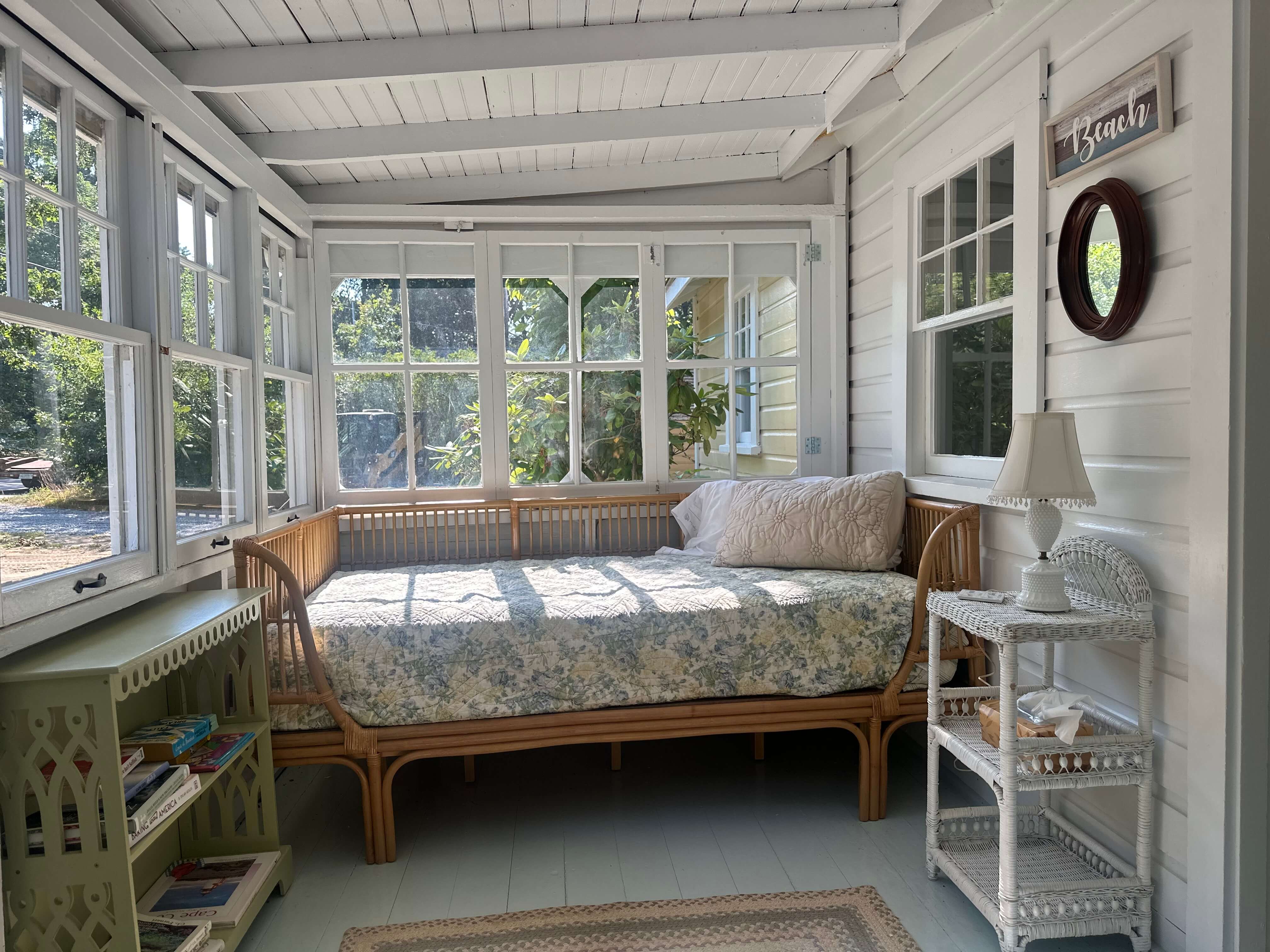 Cozy sunlit porch with a rattan daybed, decorative pillows, and a small side table.