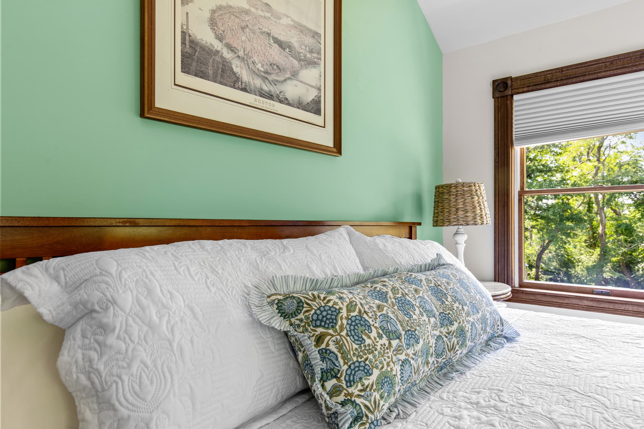 A cozy bedroom featuring a wooden bed with white bedding, a decorative pillow, and a green accent wall.