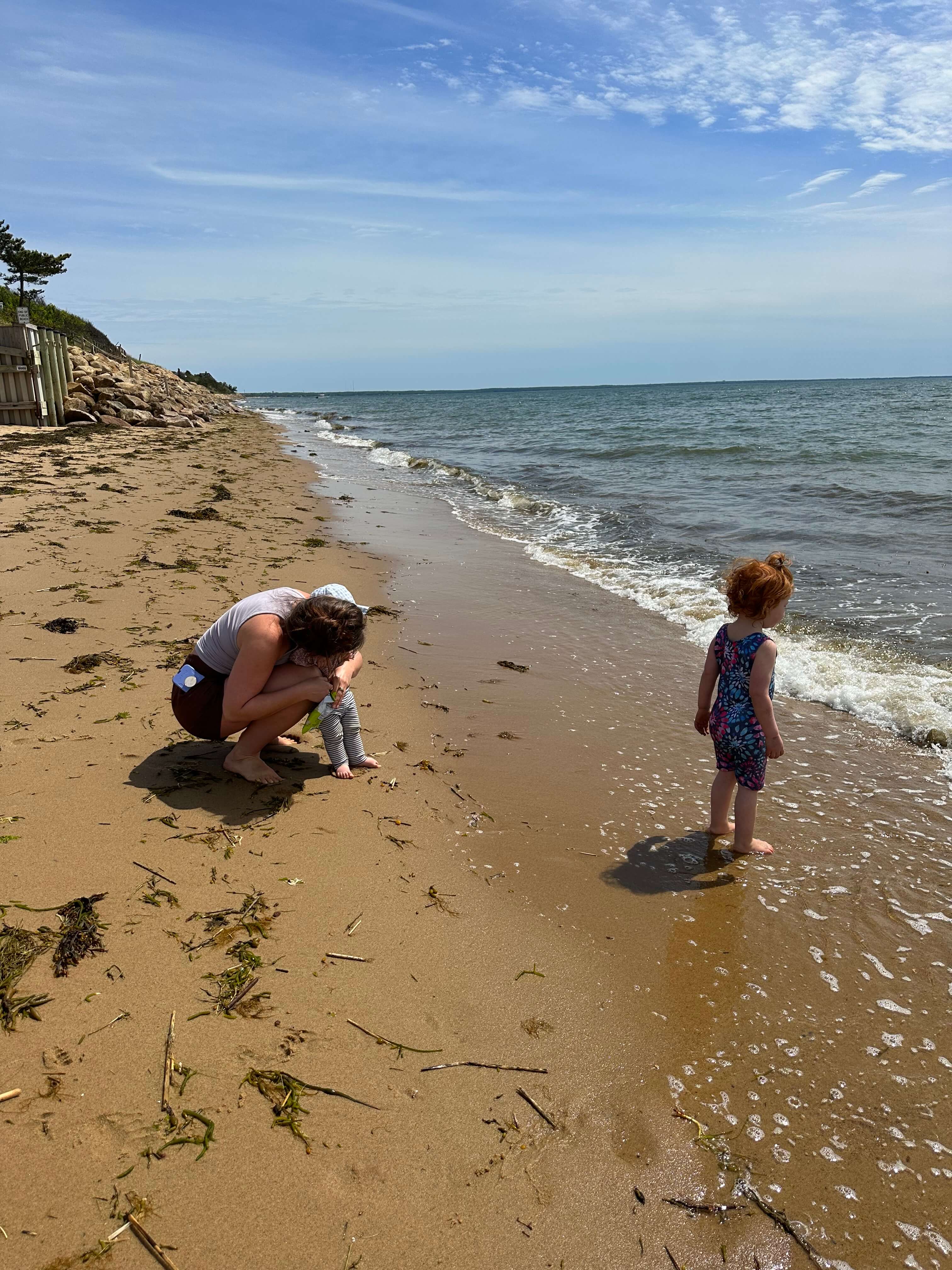A woman crouches on the beach while a young girl stands near the water's edge.