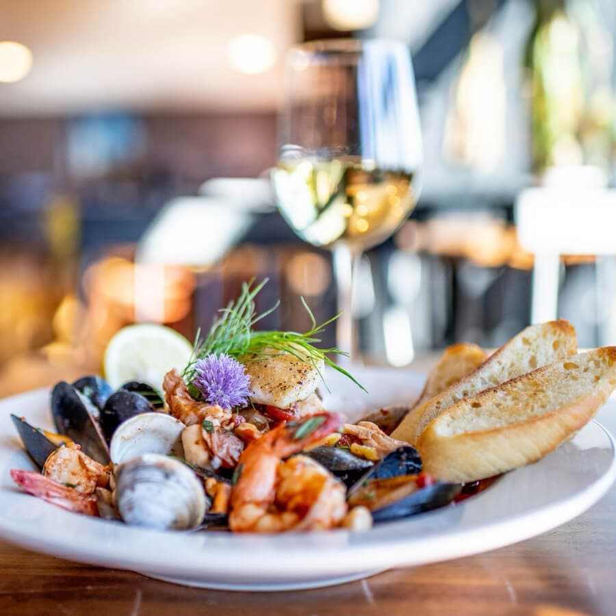 A plate of seafood with shrimp, clams, and a scallop, accompanied by toasted bread and a glass of white wine.