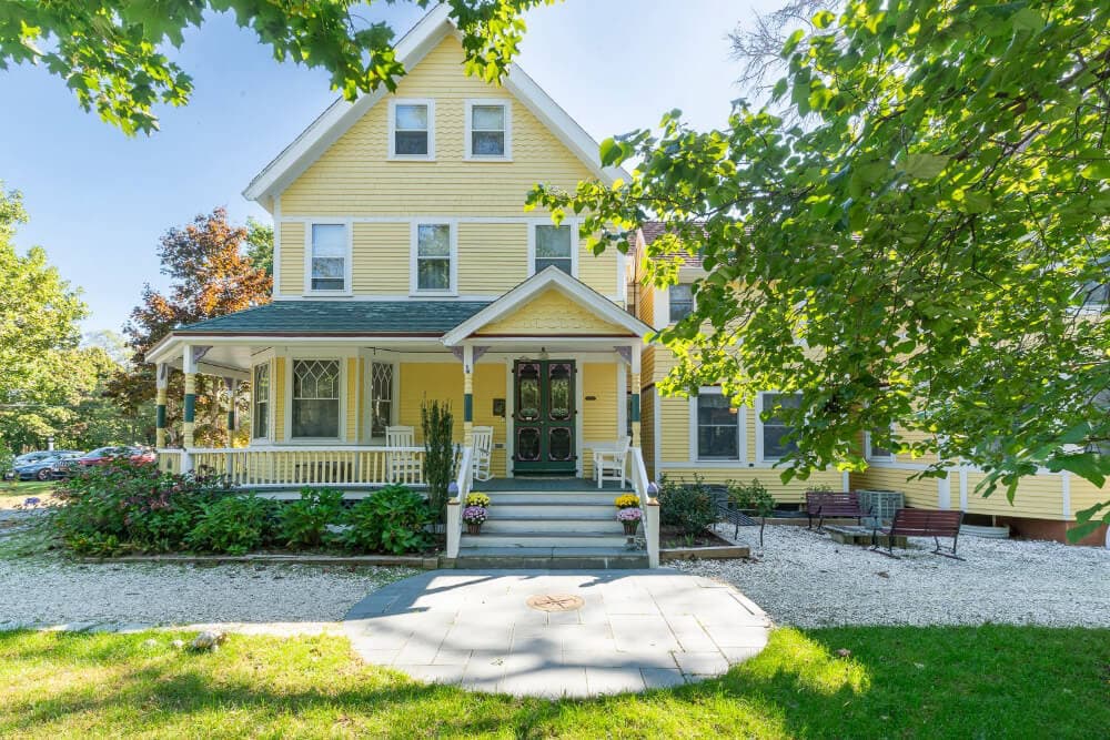 A large yellow house with a front porch surrounded by greenery.