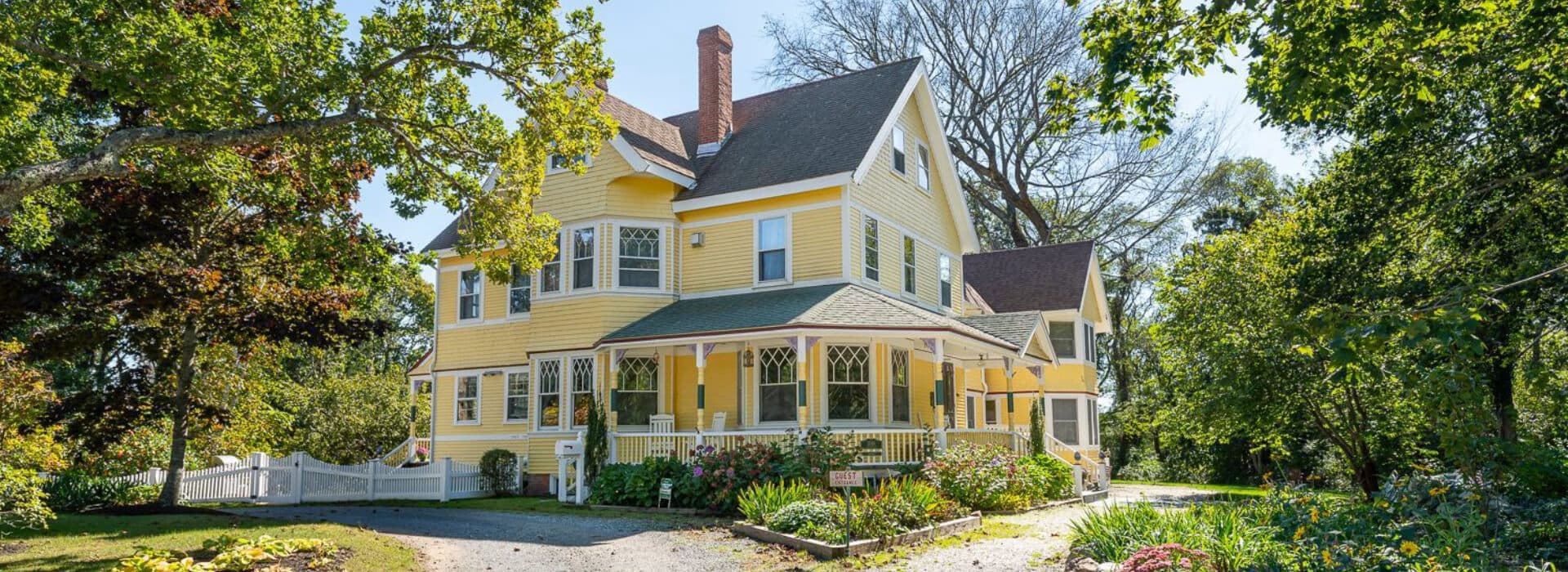 A charming yellow Victorian house surrounded by greenery.