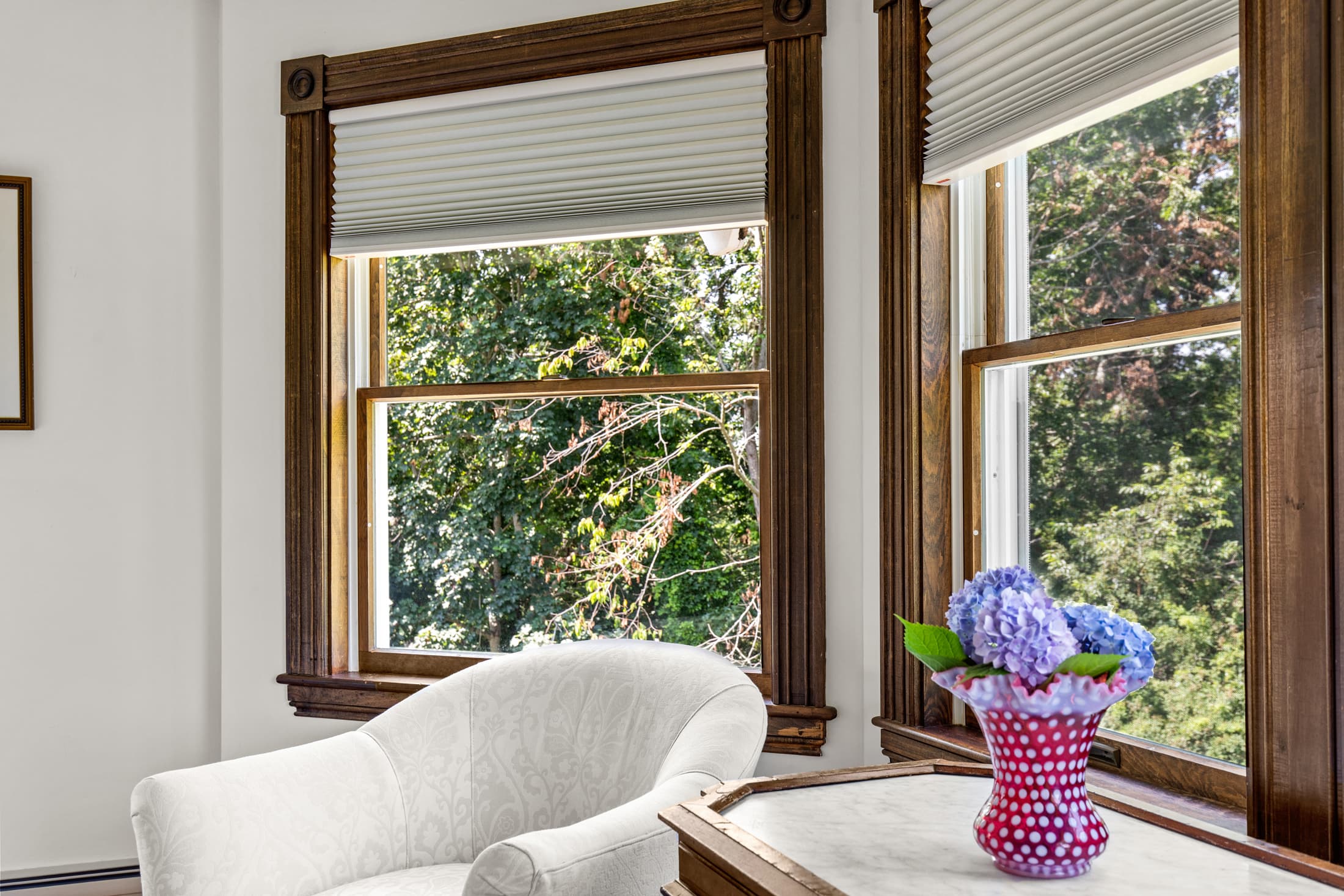Bright room with large windows, a white chair, and a vase of blue flowers on a table.