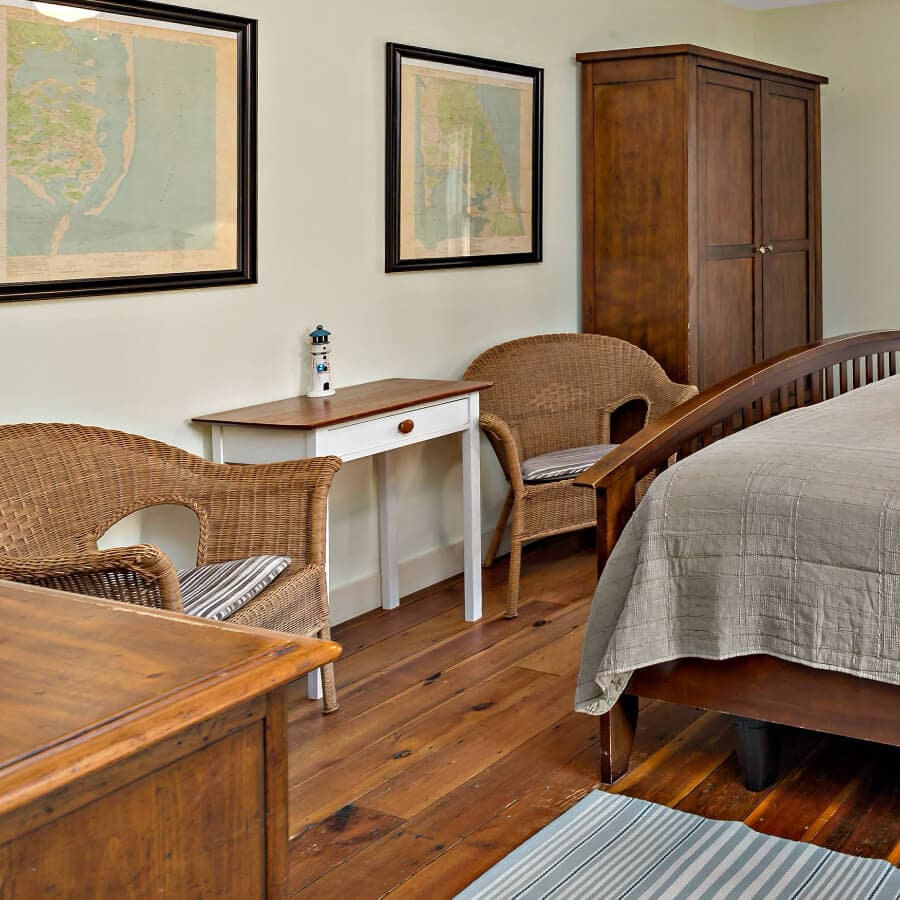 A cozy bedroom featuring a wooden bed, two wicker chairs, and framed maps on the walls.