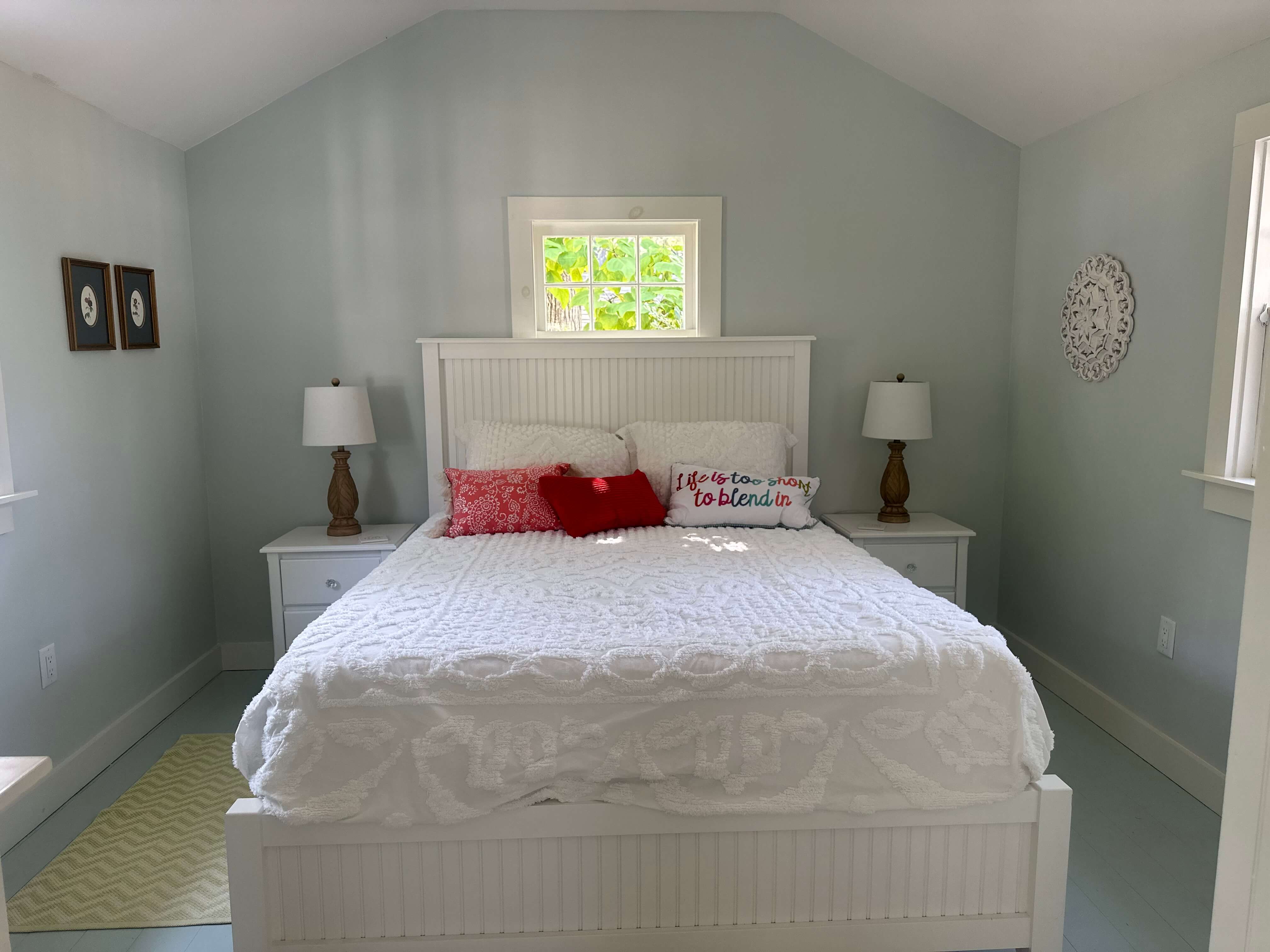 A cozy bedroom featuring a white bed with decorative pillows, two bedside lamps, and light blue walls.