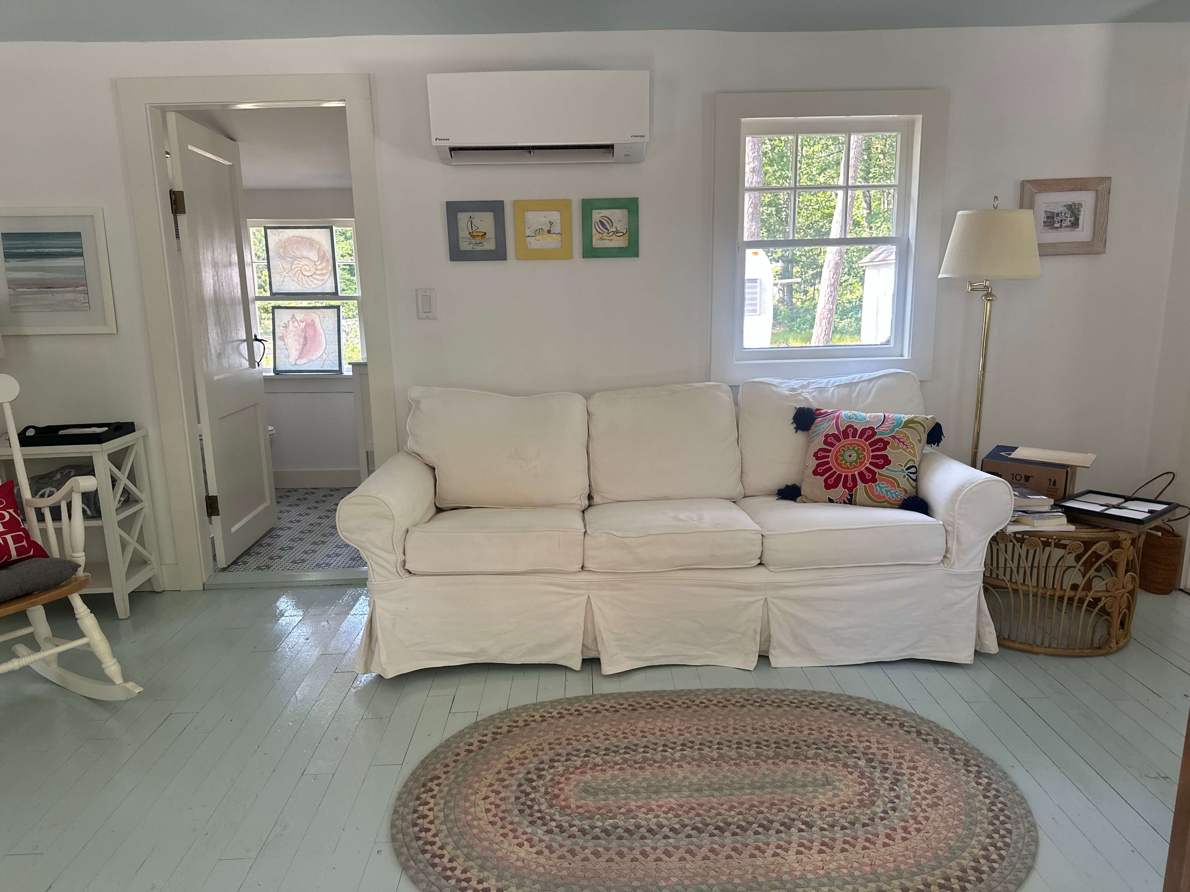 A cozy living room featuring a white sofa, colorful wall art, and a braided rug on light blue flooring.