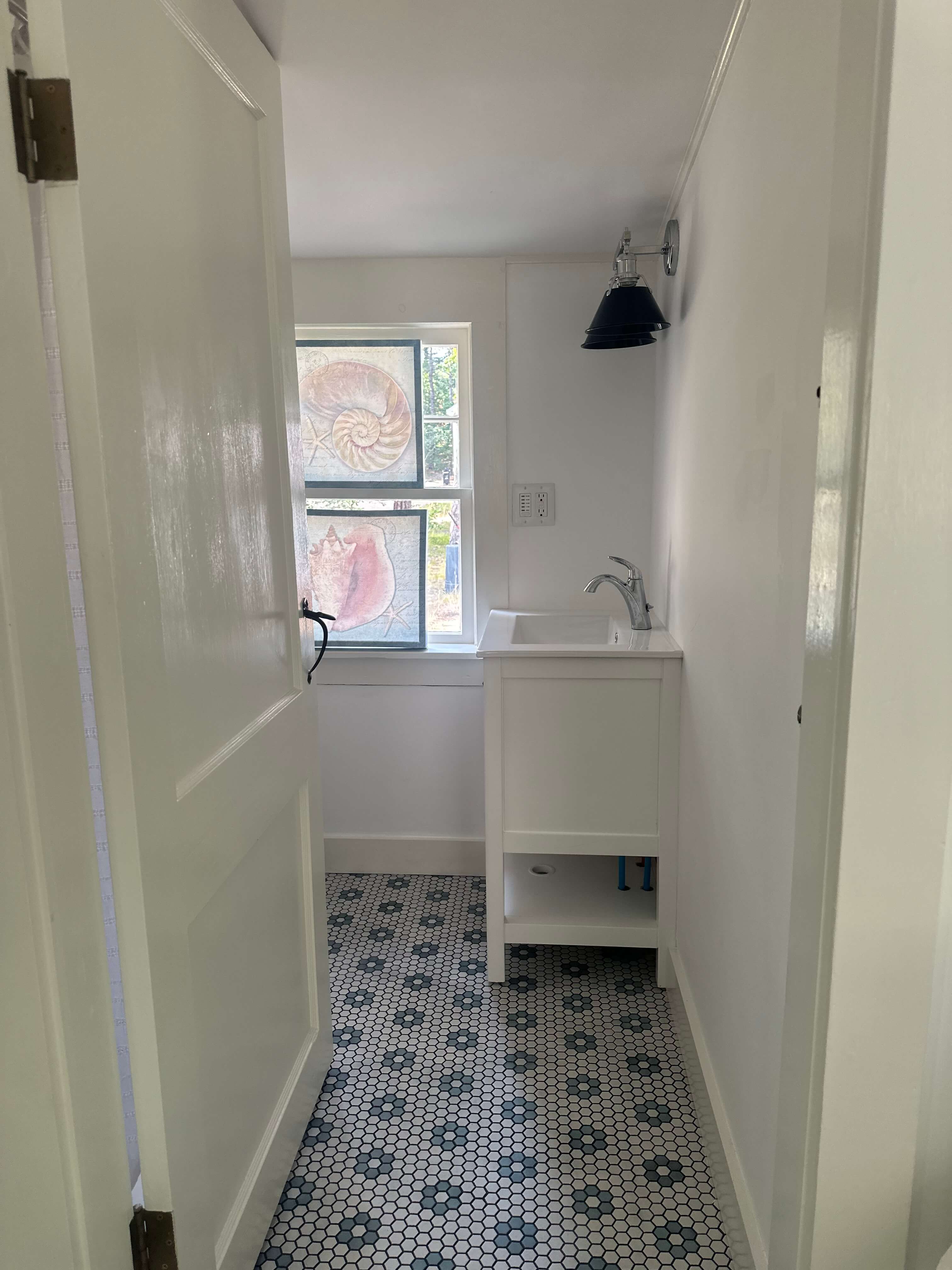 A clean, minimalist bathroom with a sink, patterned tile floor, and a window featuring decorative glass.