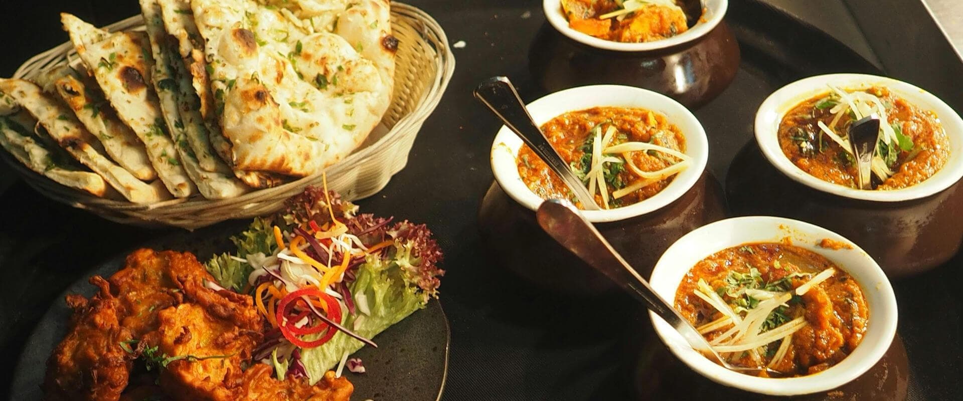 A platter of Indian dishes featuring naan bread, curry in bowls, and a salad garnish.