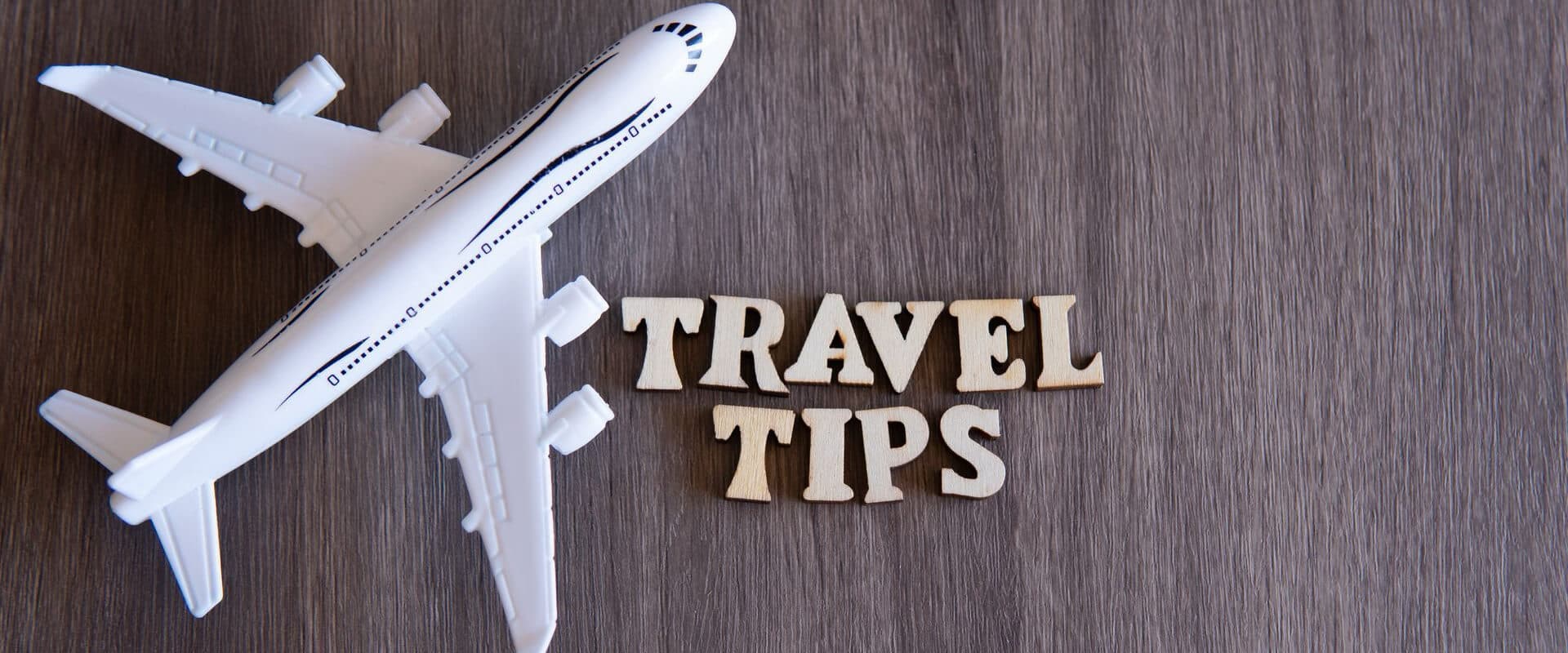 A toy airplane next to wooden letters spelling "TRAVEL TIPS."