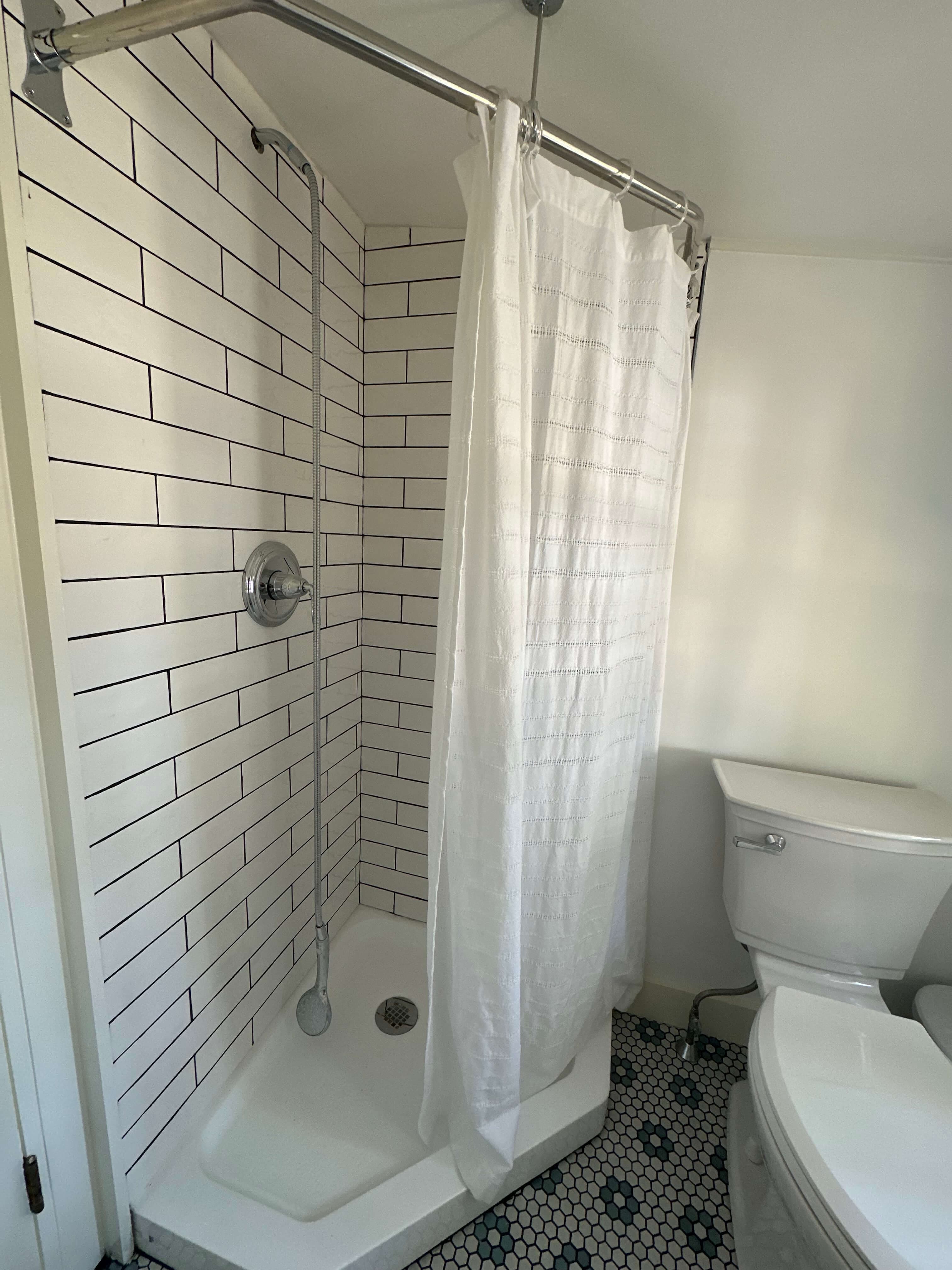 A clean, tiled shower area with a white curtain next to a toilet in a bathroom.