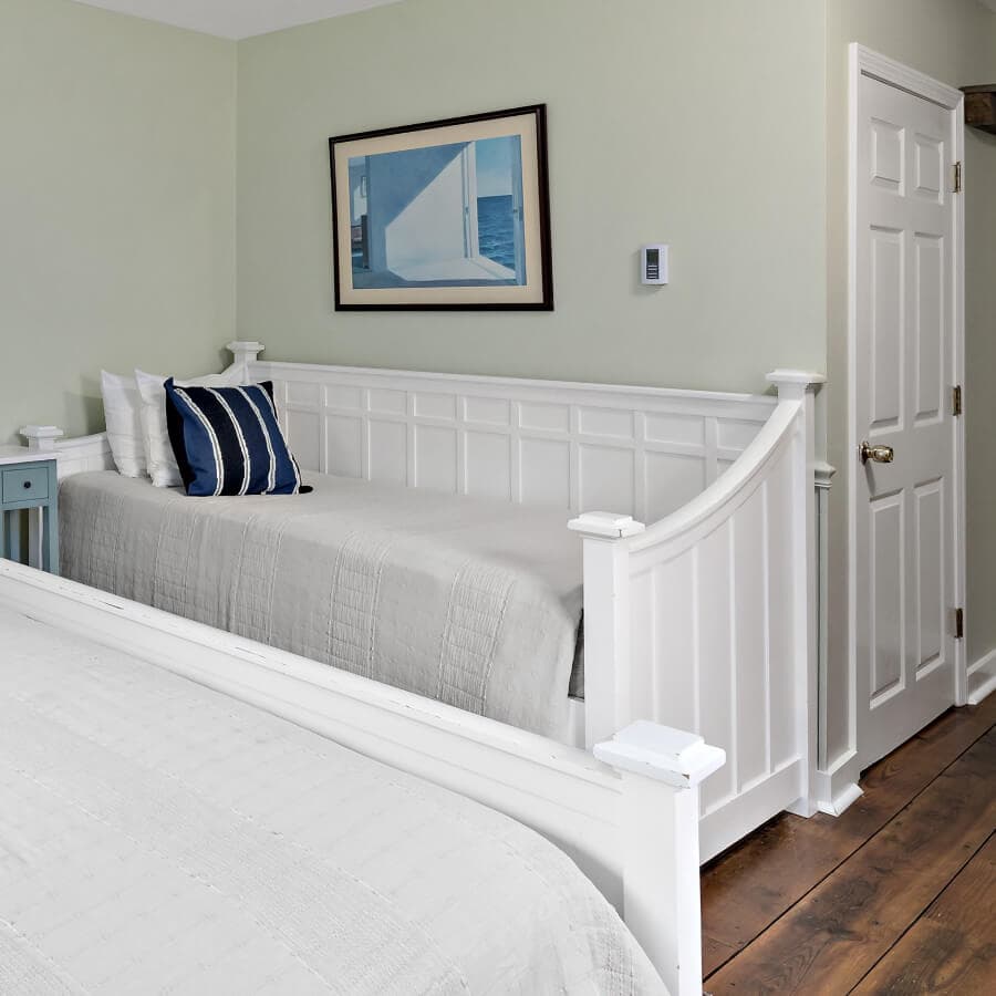 A cozy bedroom featuring a white daybed with navy striped pillows and a framed painting on the wall.