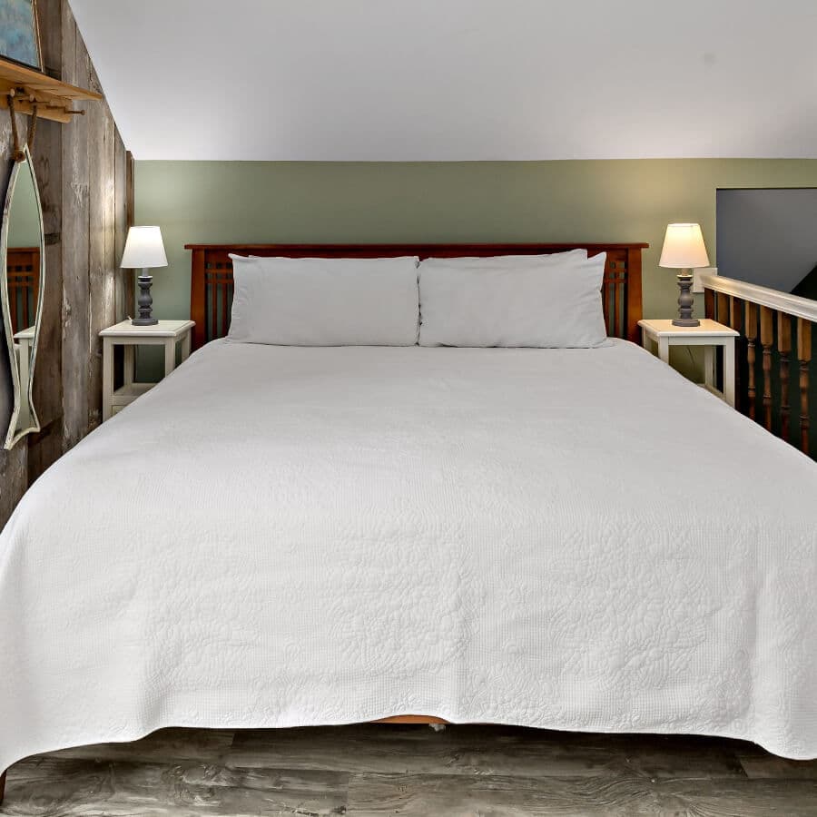 A neatly made bed with a white quilt and pillows, flanked by two bedside lamps in a cozy room.