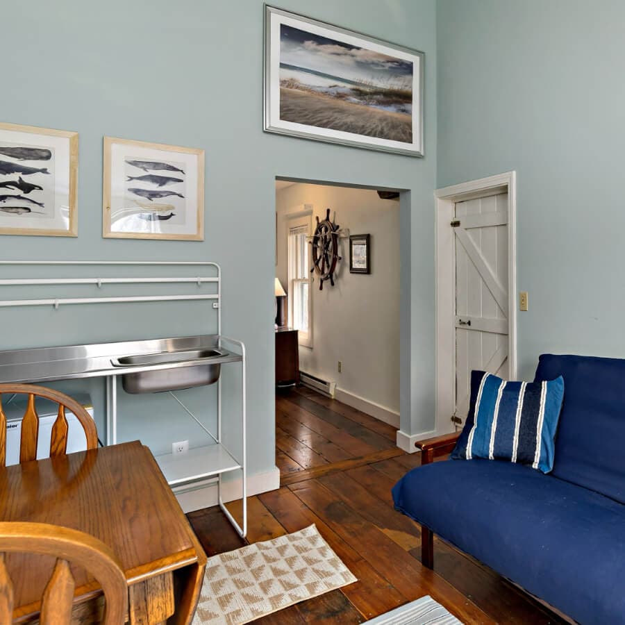 A cozy, light blue room featuring a wooden dining table, a blue sofa, fish-themed wall art, and an open doorway leading to another space.