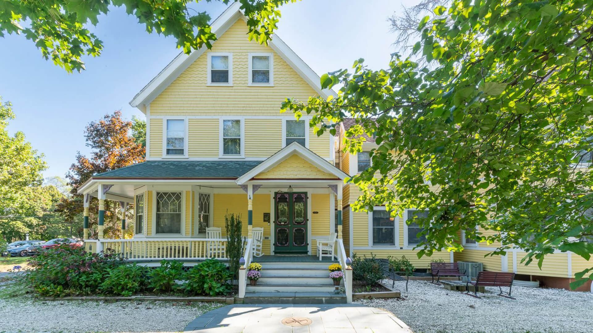 A charming yellow house with a front porch surrounded by greenery.