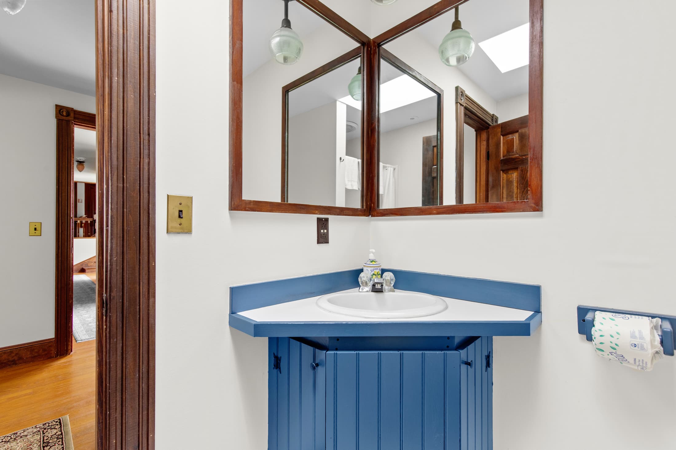 A small bathroom featuring a blue countertop sink and a mirror above, with wood accents and light fixtures.