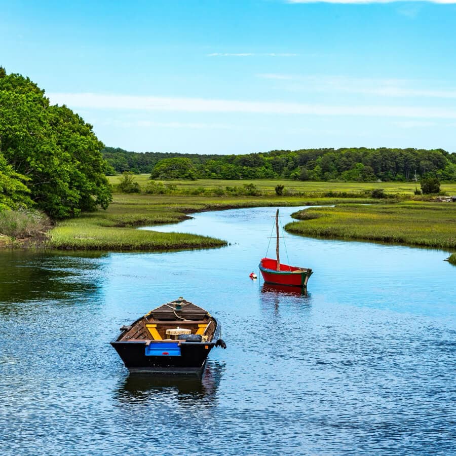 Two boats float on a winding river surrounded by lush green vegetation under a clear blue sky.