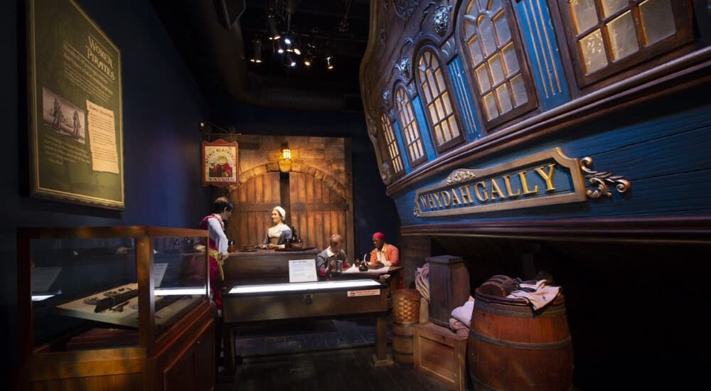 A historical exhibit featuring a ship model, artifacts, and costumed figures in an atmospheric setting.