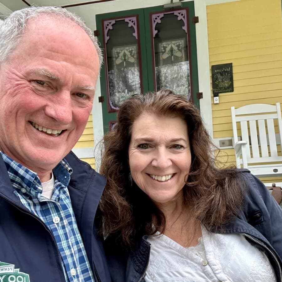 A man and a woman smile at the camera while posing in front of a colorful house.