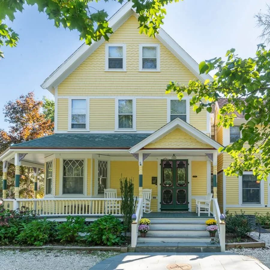 A charming yellow Victorian house with a front porch and colorful flowers in the garden.