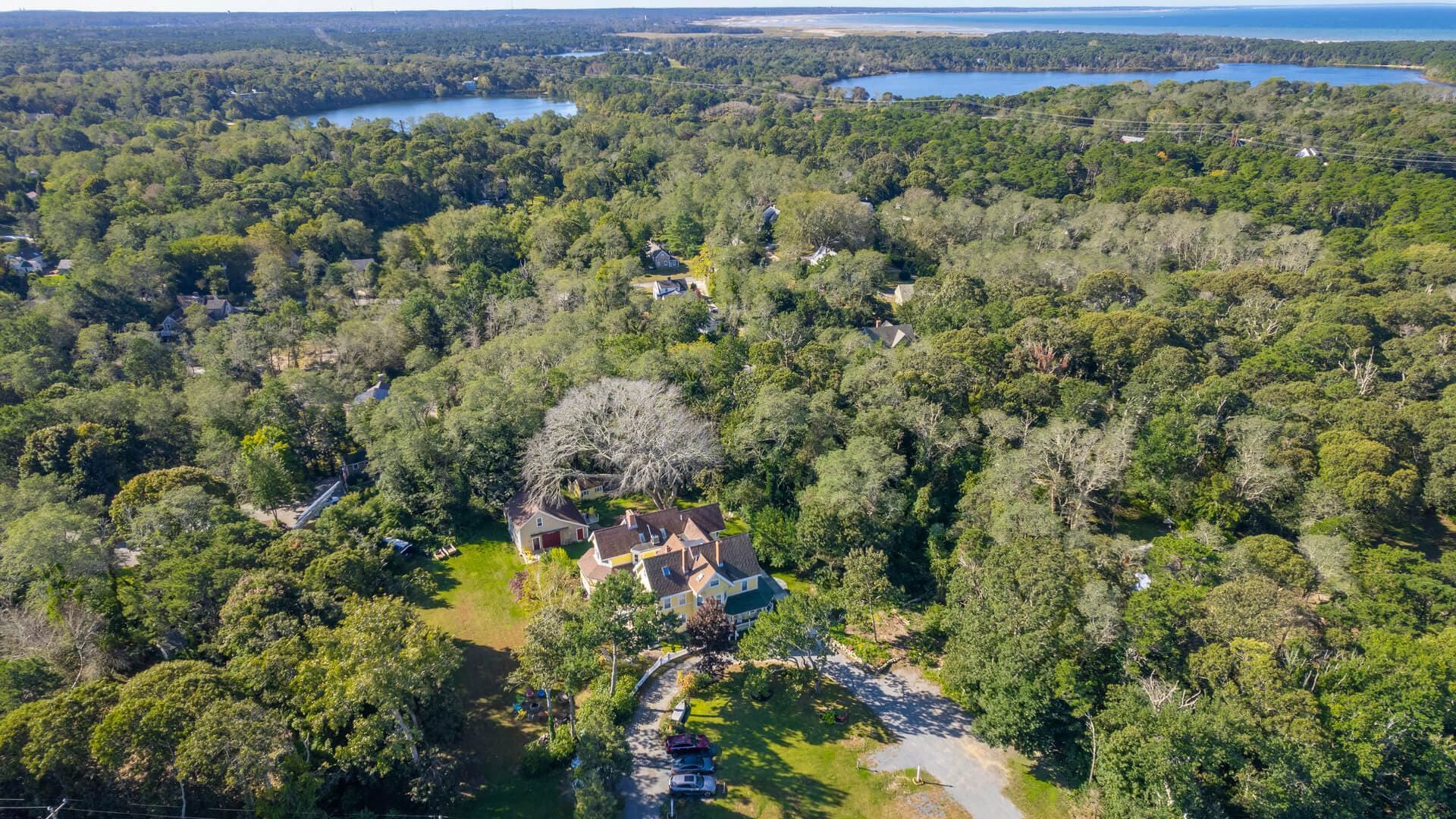 An aerial view of a wooded area featuring a cluster of houses and nearby lakes.