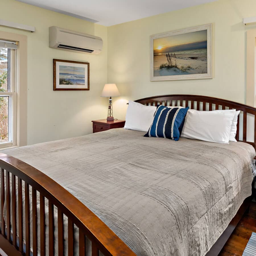 A cozy bedroom featuring a wooden bed, light-colored walls, a lamp, and beach-themed artwork.