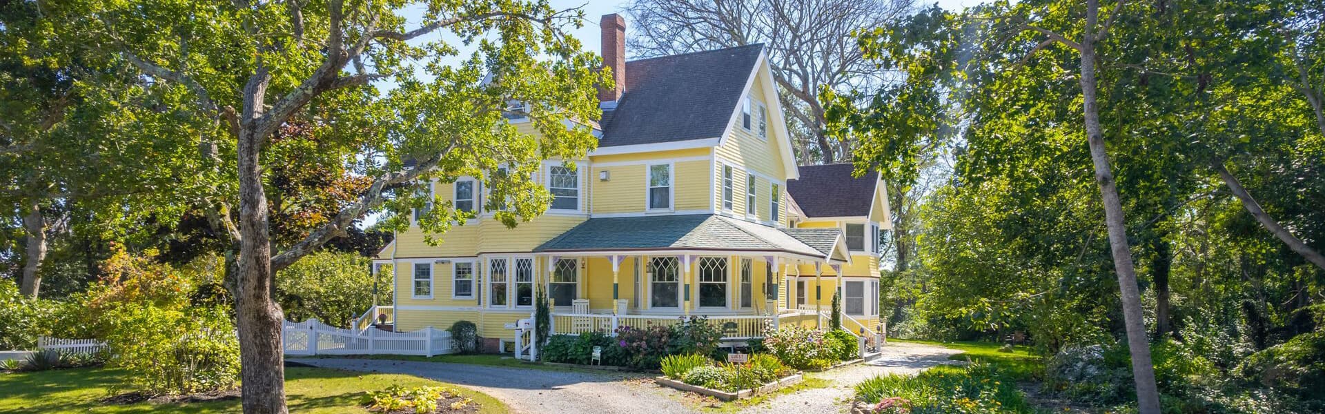 A charming yellow Victorian house surrounded by lush trees and greenery.