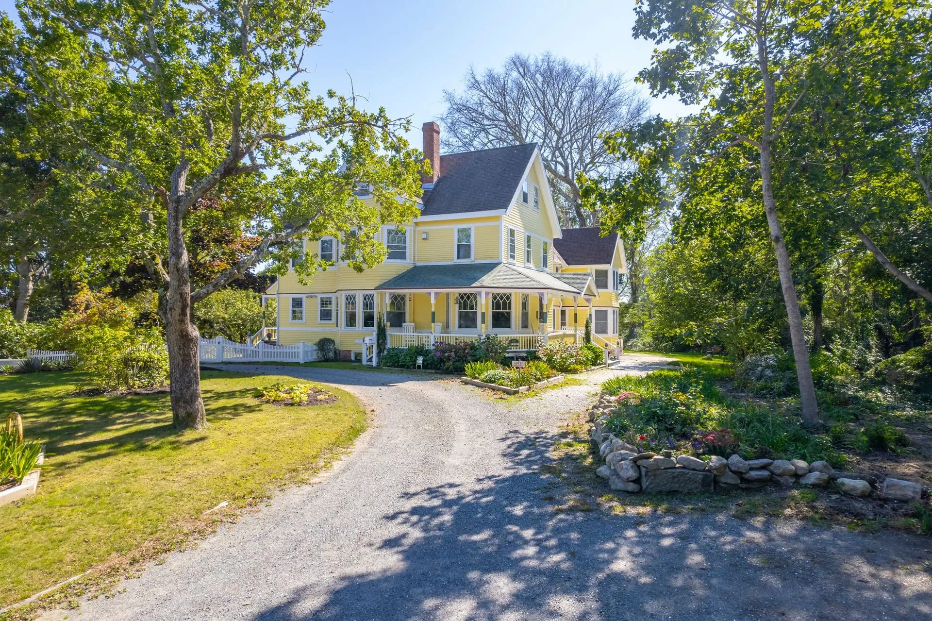 A charming yellow Victorian house surrounded by lush greenery and a gravel driveway. A charming yellow Victorian house surrounded by lush greenery and a gravel driveway.