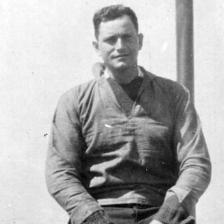 A man in a vintage sports jersey sits casually against a backdrop.