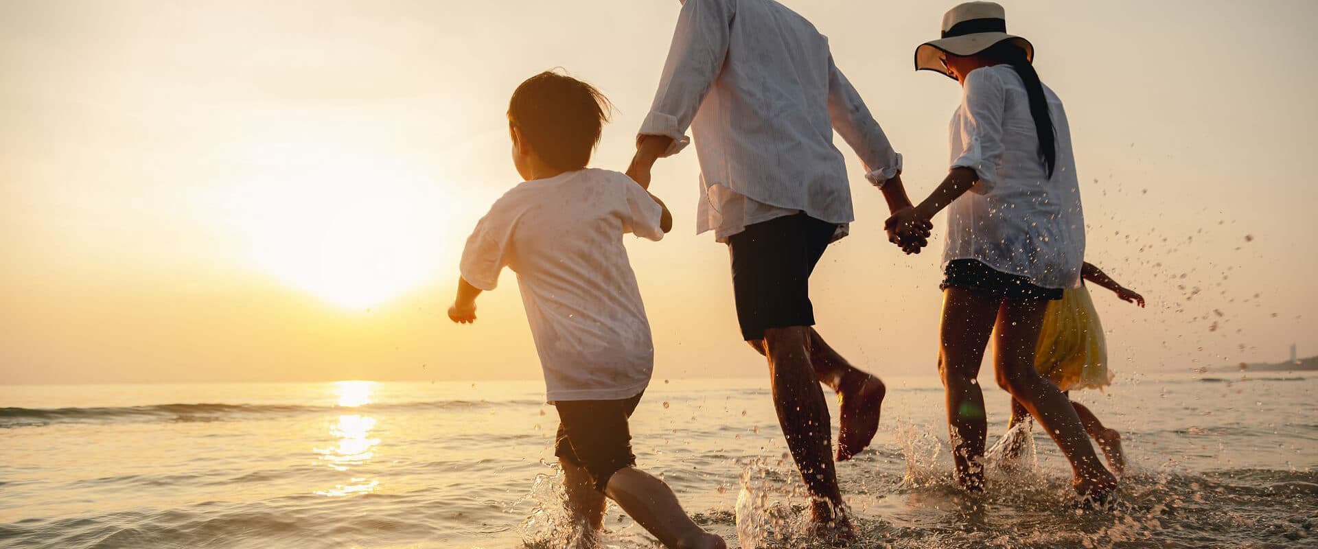 A family wades through the water at sunset, enjoying a playful moment together.