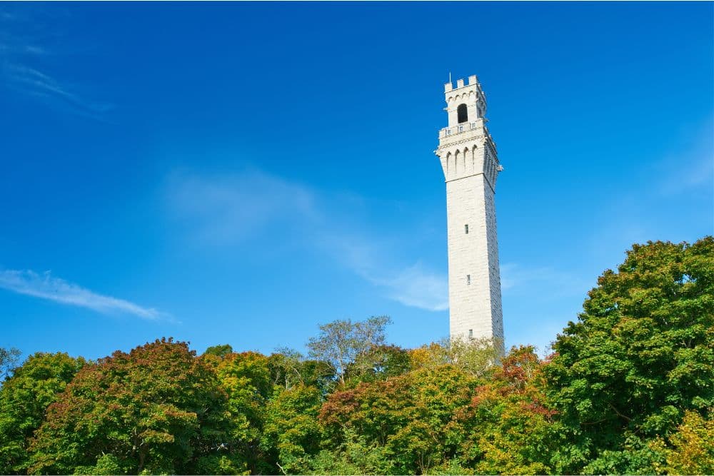 A tall stone tower rises above colorful trees under a clear blue sky.