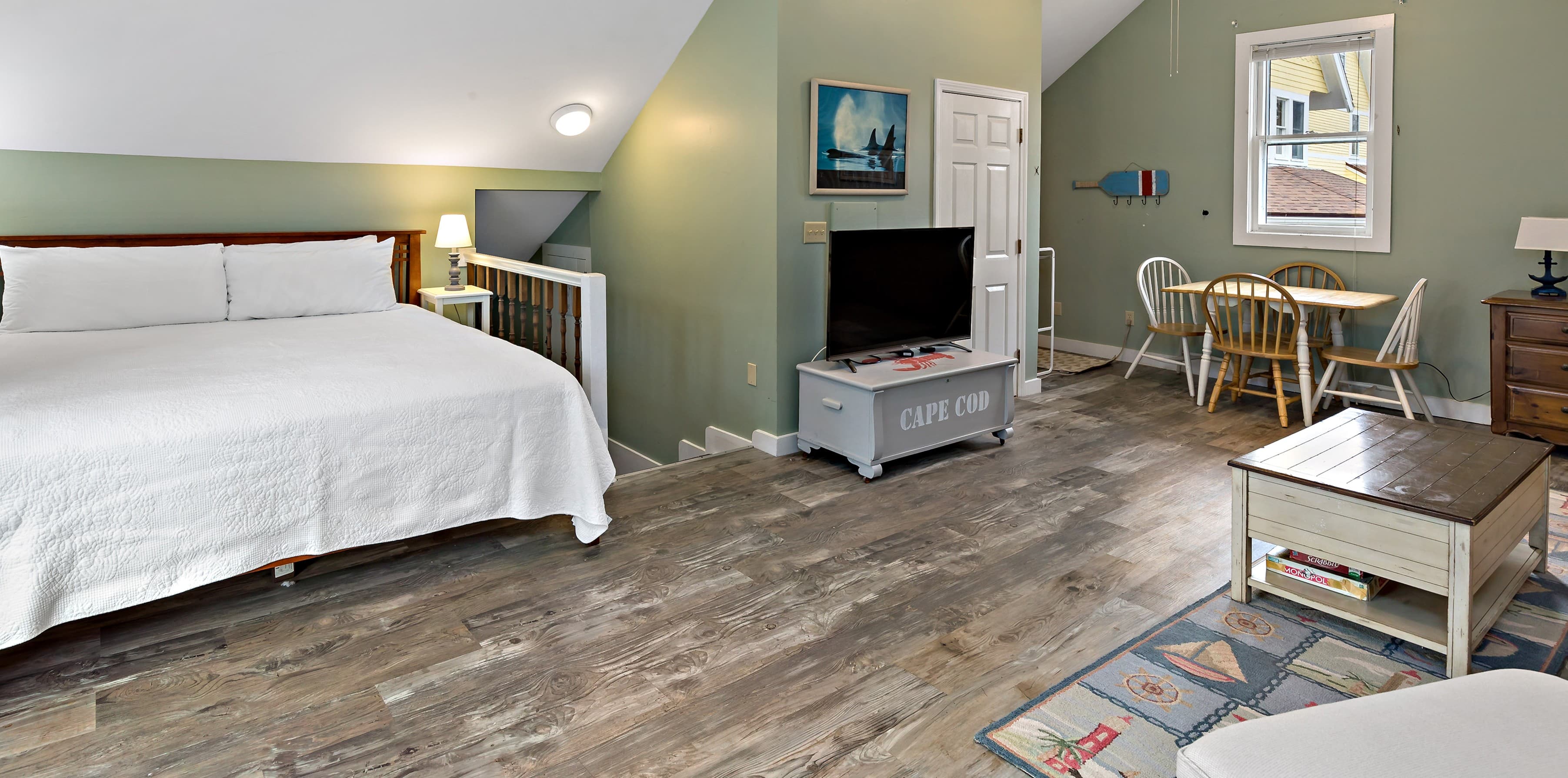 Cozy attic bedroom featuring a large bed, TV, dining area, and hardwood flooring.