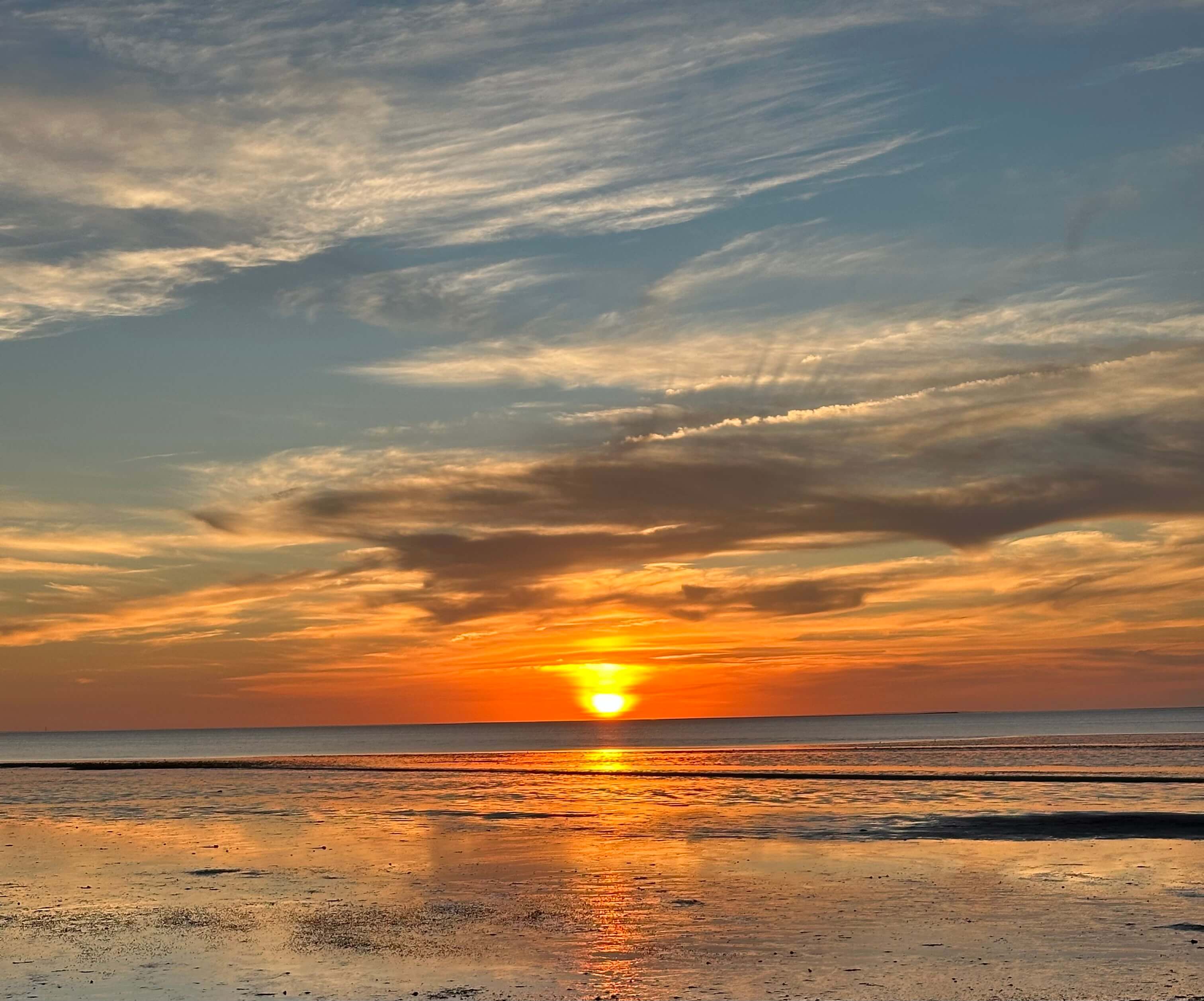 A vibrant sunset reflecting on calm water with scattered clouds in the sky.