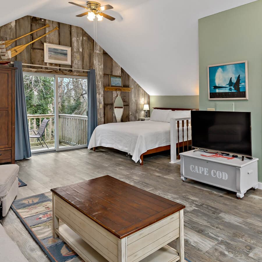 Cozy bedroom with a wooden accent wall, a bed, a TV, and sliding glass doors leading to a balcony.
