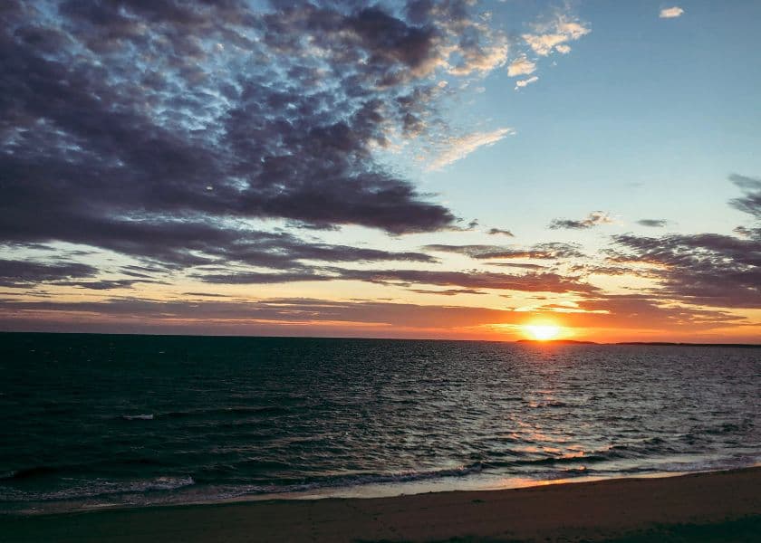 A Cape Cod beach at sunset with dramatic clouds, ocean waves, and golden light on the horizon.