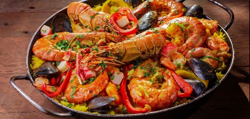 A skillet of seafood paella with shrimp, lobster, mussels, peppers, herbs, and yellow rice.